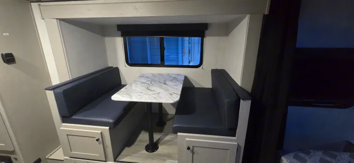 Inside an RV rental: a modern dinette featuring comfy blue benches, a marble-style table, and a window.. Coachmen Apex 2025