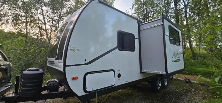 An RV rental, this white Apex Nano travel trailer is parked at a shady campsite with its slide-out open.. Coachmen Apex 2025