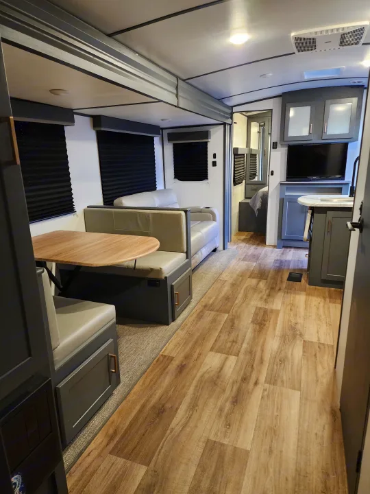A bright, modern RV rental interior featuring a practical dinette, kitchen, and living area, with wood-look floors.. Keystone RV Bullet Ultra Lite 2023