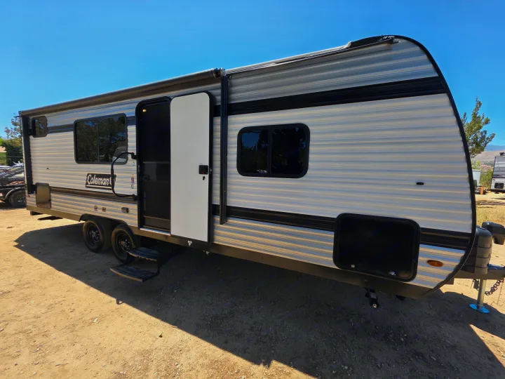 Grey Coleman travel trailer with an open door, parked on dirt. Perfect for your next rv rental adventure.. Keystone Coleman 2025