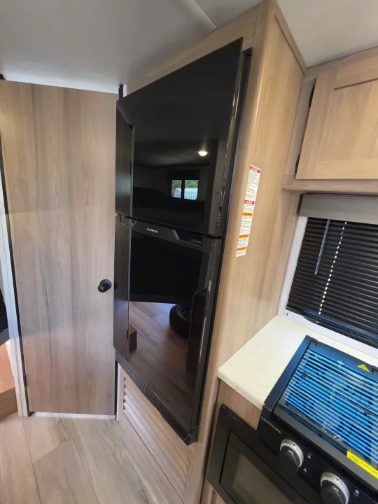 RV rental interior with modern kitchen appliances, including a Furrion fridge and Greystone stovetop, next to a wooden door.. Keystone Coleman 2025