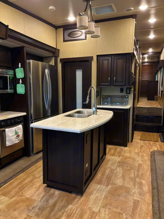Spacious RV rental kitchen with modern dark wood cabinets, a full-size stainless steel fridge, and an island with a sink.. 4x4fcmp23h6007284 Columbus 2017