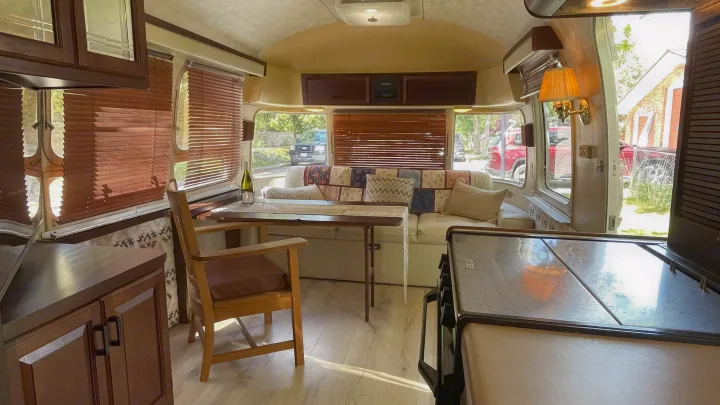 Inside a cozy RV rental: light wood floor, dinette with table, upholstered sofa, and wood blinds create a bright, inviting space.. Airstream Excella 1990