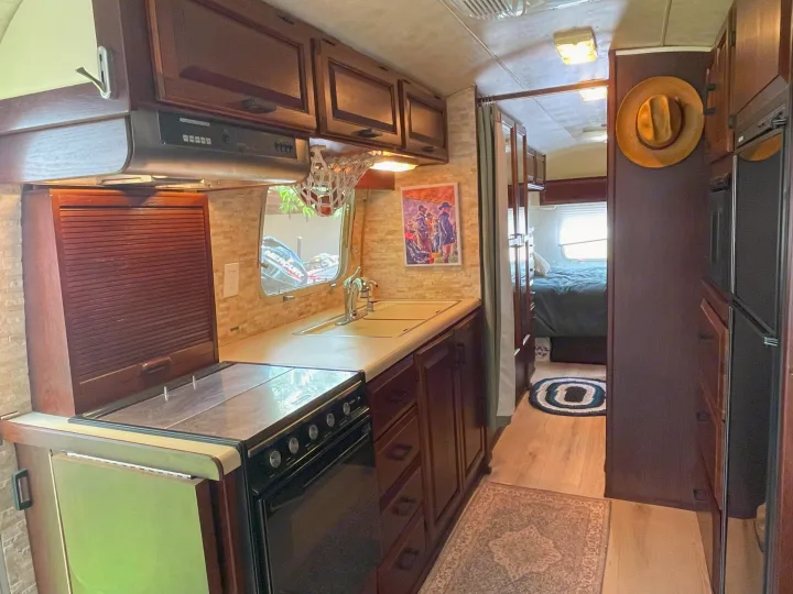 This rv rental features a functional kitchen/galley with oven, sink, and fridge, leading to a cozy bedroom.. Airstream Excella 1990