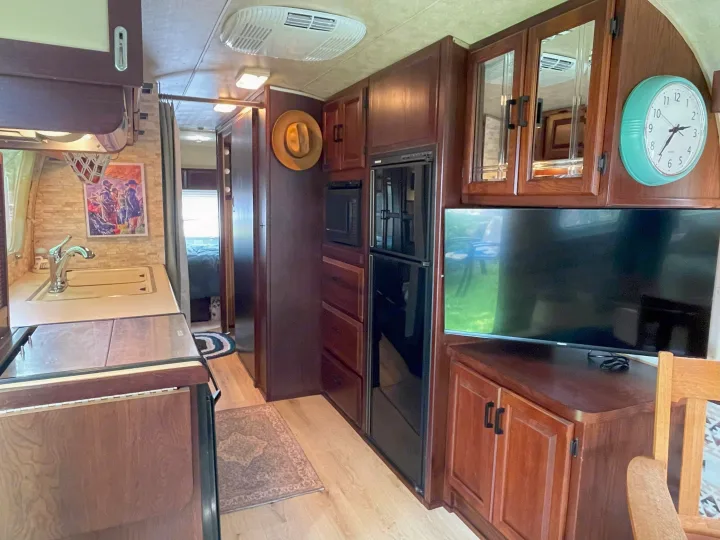 Inside RV rental: well-equipped kitchen, fridge, microwave, and TV area with wood cabinetry. View extends to the back bedroom.. Airstream Excella 1990