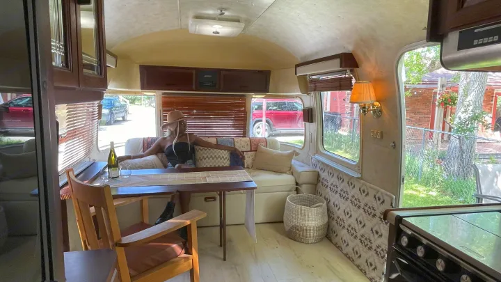 Serene RV rental interior: a woman unwinds on the sofa, with a dining table, wine, and full kitchen visible.. Airstream Excella 1990