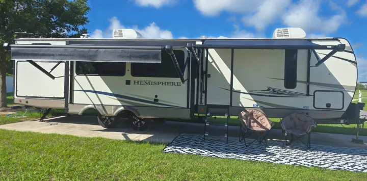 This Forest River Hemisphere rv rental is set up on a sunny pad with an awning, chairs, and mat for a relaxing outdoor stay.. Forest River Salem Hemisphere 2021