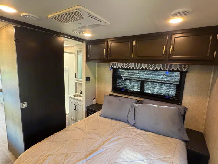Inside an RV rental, this cozy bedroom features a quilted bed, overhead cabinets, and a sliding door to the compact bathroom.. Entegra Coach Odyssey 2022