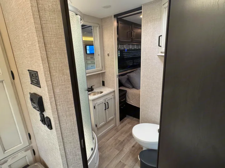 Inside an RV rental: a compact bathroom with a shower, sink, and toilet, leading to a cozy bedroom.. Entegra Coach Odyssey 2022