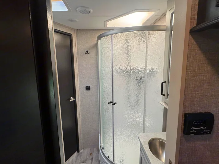 Compact RV rental bathroom with a curved shower, vanity sink, and controls like the Coleman-Mach thermostat.. Entegra Coach Odyssey 2022