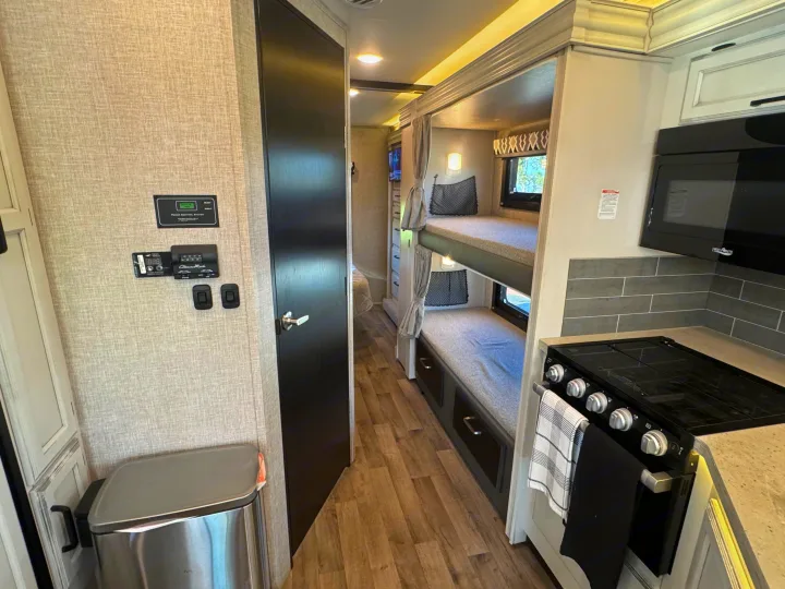 RV rental interior: A modern kitchen with stove & microwave, cozy bunk beds, and control panels on a textured wall.. Entegra Coach Odyssey 2022
