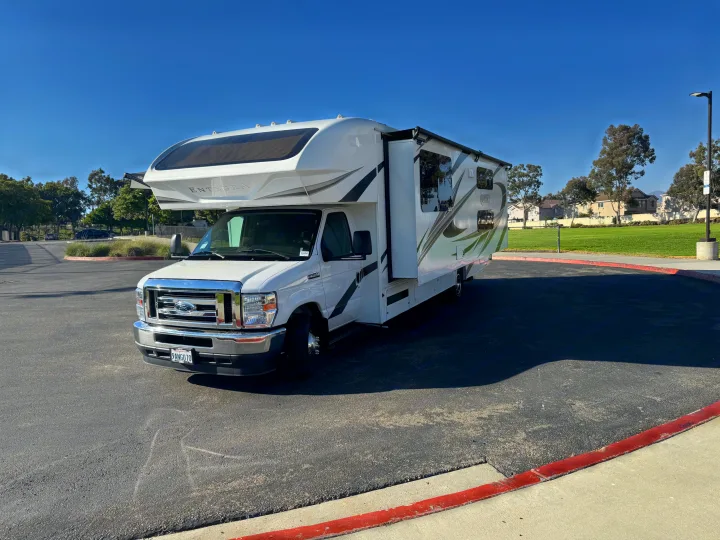 Modern white Class C RV rental, an Entegra Odyssey, parked outdoors on asphalt, bathed in sunlight.. Entegra Coach Odyssey 2022