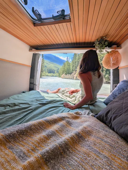 An RV rental provides a scenic escape: a person relaxes on a cozy bed, gazing at a river and mountains.. Mercedes-Benz Mercedes Sprinter 2500 2015