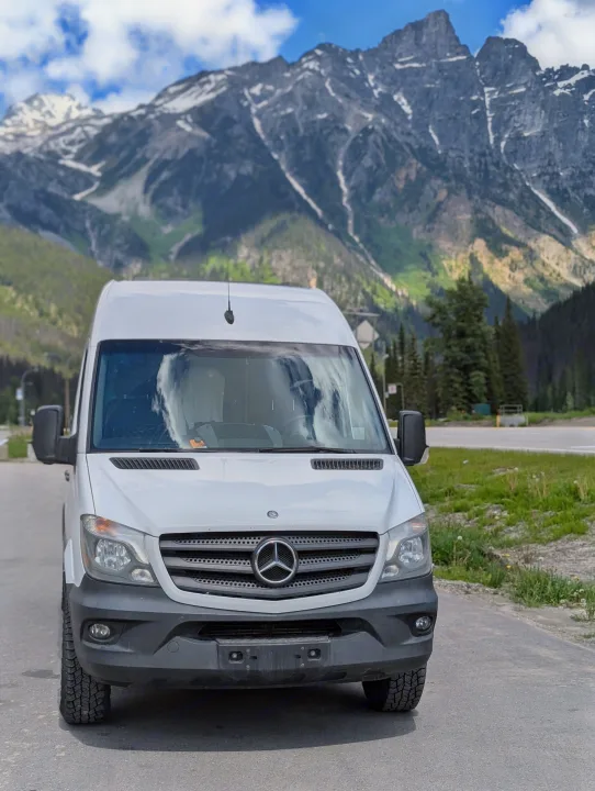 White Mercedes Sprinter RV rental van parked against a backdrop of majestic, snow-capped mountains and blue sky.. Mercedes-Benz Mercedes Sprinter 2500 2015