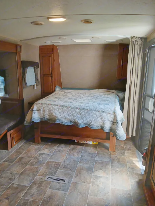 Cozy RV rental interior featuring a comfortable bed, wood cabinetry, tiled floor, and a compact living area.. Forest River Rockwood Ultra Lite 2016