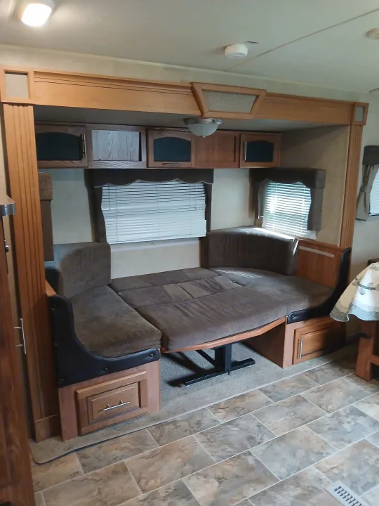 Explore this RV rental's clever interior: a dinette with brown cushions easily converts to a bed, surrounded by wood cabinetry. Ideal for travel.. Forest River Rockwood Ultra Lite 2016