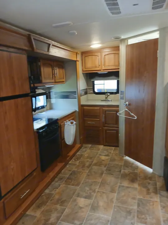 RV rental kitchen showcasing a fridge, stove, sink, wood cabinets, and tiled floor. Compact and well-equipped interior.. Forest River Rockwood Ultra Lite 2016