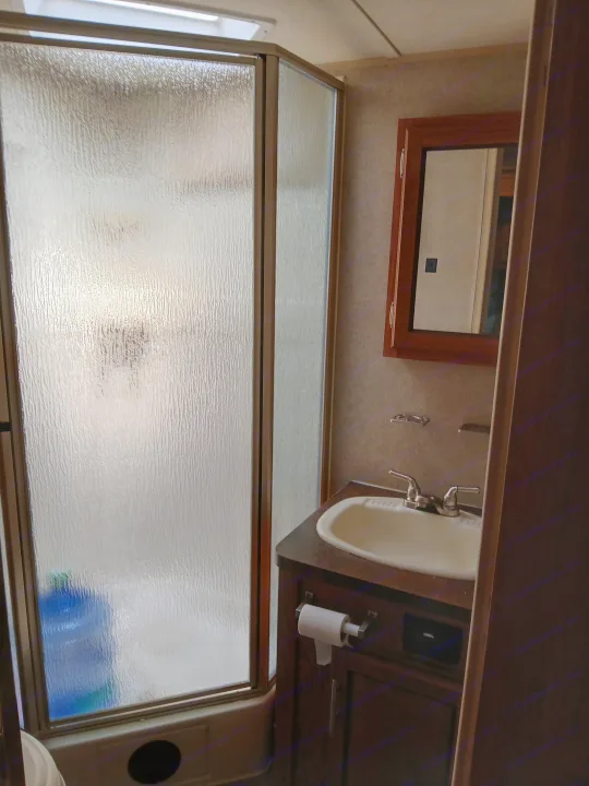Compact RV rental bathroom with frosted glass shower, sink vanity, and mirror cabinet.. Forest River Rockwood Ultra Lite 2016