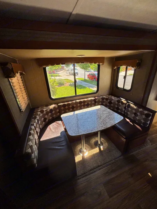RV rental interior featuring a cozy dinette with U-shaped seating and a table, brightened by sunlight through the windows.. Keystone Passport 2016