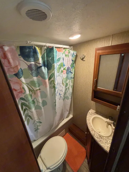 Inside an RV rental bathroom with a floral shower curtain, toilet, and sink. A compact yet functional space.. Keystone Passport 2016