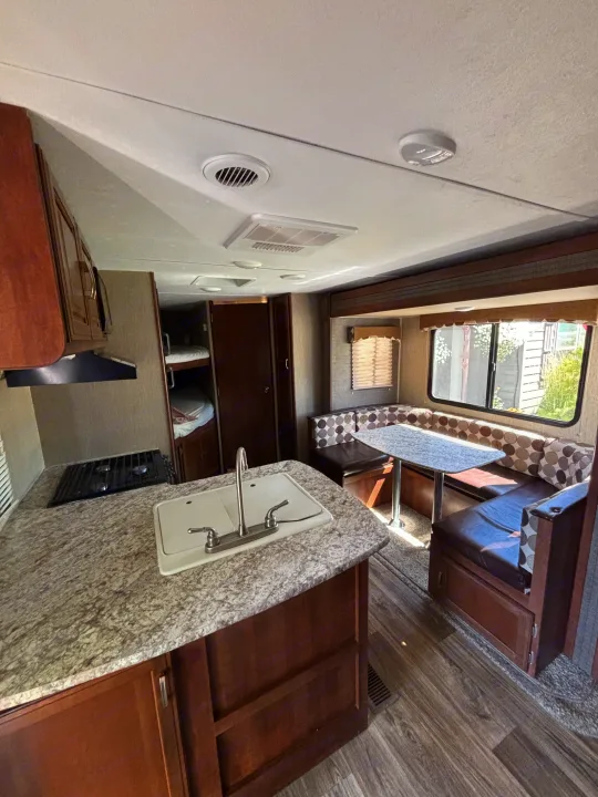 RV rental interior features a kitchen with a sink and stovetop, a U-shaped dining booth with patterned cushions, and bunk beds.. Keystone Passport 2016