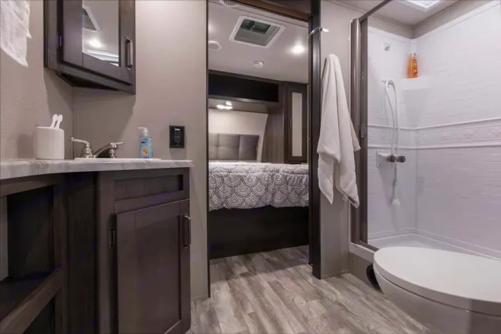 This RV rental offers a well-equipped bathroom with a vanity, sink, shower, and toilet, connecting to a cozy bedroom.. xpolar 265bh 2023