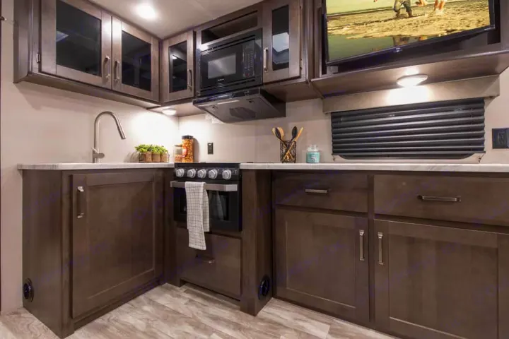Spacious RV rental kitchen featuring modern dark cabinetry, a full stove, microwave, sink, and overhead TV.. xpolar 265bh 2023