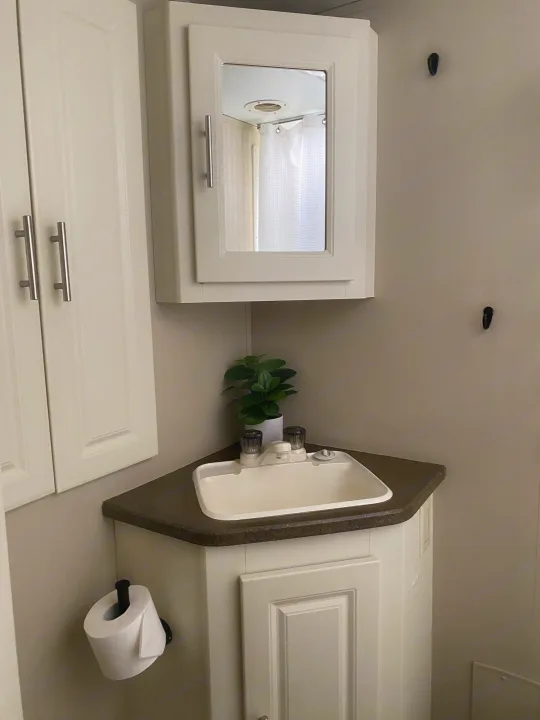 RV rental bathroom featuring a corner sink, mirrored cabinet reflecting the shower, toilet paper holder, and wall hooks.. Cruiser RV Fun Finder X 2011