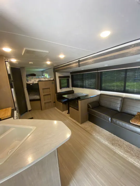 RV rental interior showcasing a well-lit living space with a kitchen sink, bunk beds, dinette, and sofa seating.. Keystone RV Hideout 2021