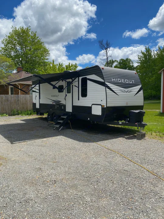 Modern Hideout travel trailer RV rental, with awning out, parked on gravel under bright blue skies.. Keystone RV Hideout 2021