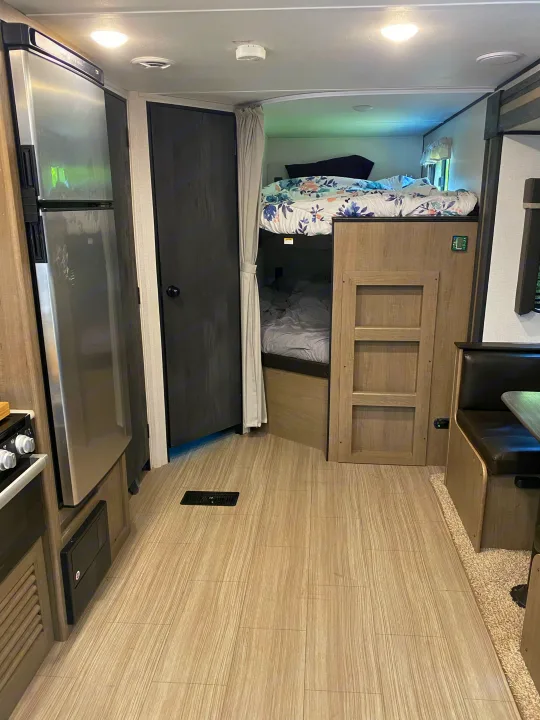 RV rental interior showcasing a stainless steel fridge, bunk beds with floral bedding, and a cozy dinette setup.. Keystone RV Hideout 2021