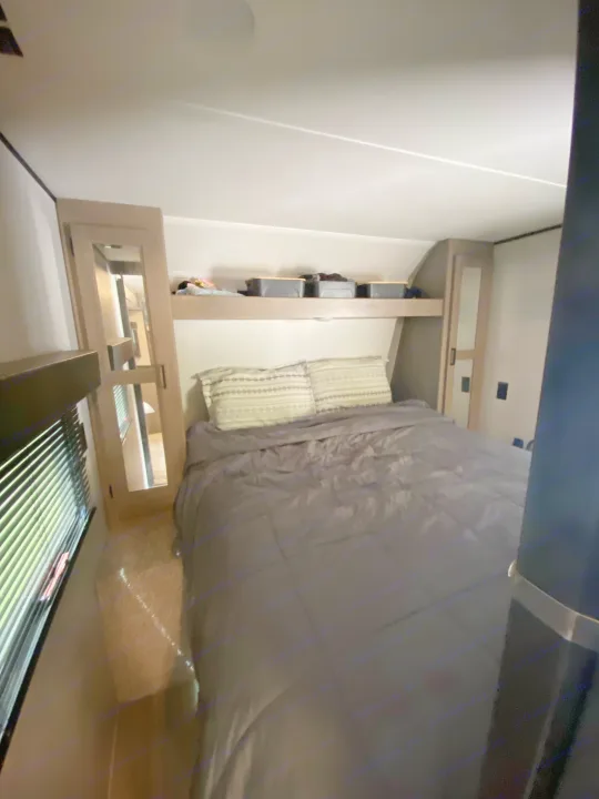 A view inside a typical RV rental bedroom, featuring a bed, overhead storage, and mirrored closets.. Keystone RV Hideout 2021