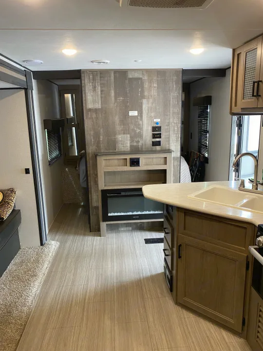 Modern RV rental interior showcasing a well-lit kitchen, living space with a fireplace, and hallway access.. Keystone RV Hideout 2021
