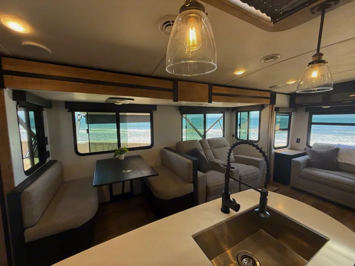 Enjoy this spacious RV rental interior with stunning beach views, featuring comfortable living, dining, & kitchen areas.. Keystone RV Outback 2022