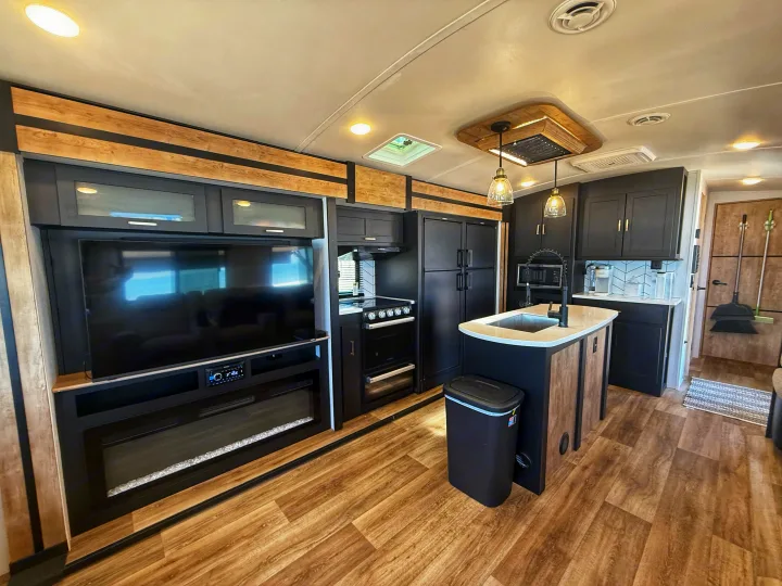 Well-equipped RV rental kitchen and living area with black appliances, island, TV, and fireplace.. Keystone RV Outback 2022