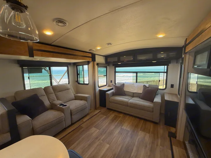 Enjoy the ocean view from this comfortable RV rental living space, featuring sofas and large windows.. Keystone RV Outback 2022