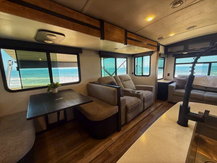 Spacious RV rental interior with stunning ocean view, featuring dining, living, and kitchen areas for a comfortable beach getaway.. Keystone RV Outback 2022