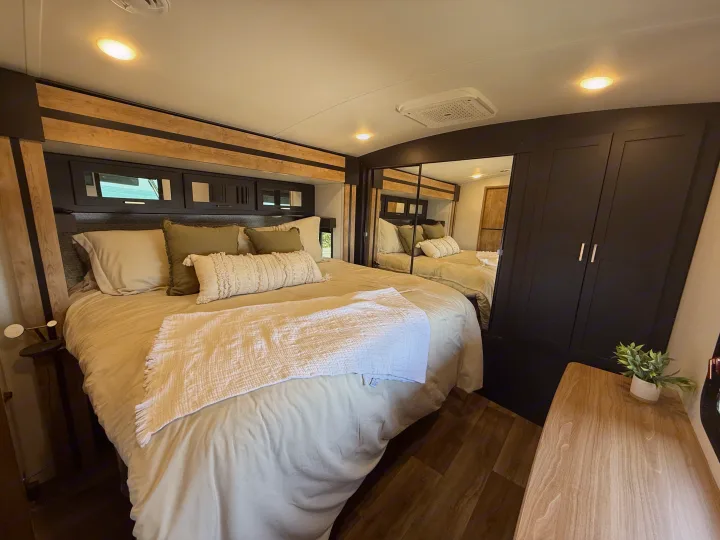 Modern RV rental bedroom featuring a large bed, stylish dark cabinets, mirrored closet, and wood flooring.. Keystone RV Outback 2022