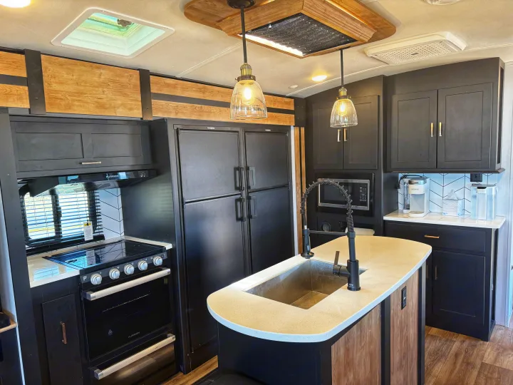Modern RV rental kitchen with black cabinets, light counters, wood accents, & full appliances for a comfortable stay.. Keystone RV Outback 2022