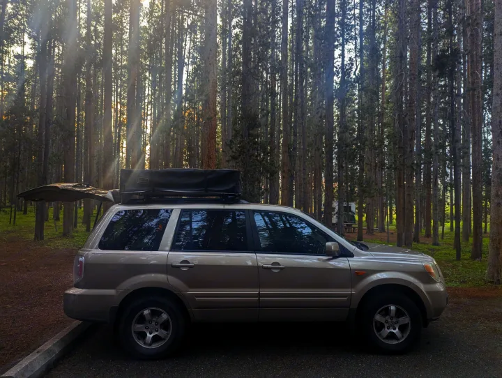 Beige SUV with open hatch & rooftop tent at a peaceful forest campsite. An agile alternative to an RV rental for nature adventures.. Honda Pilot 2007