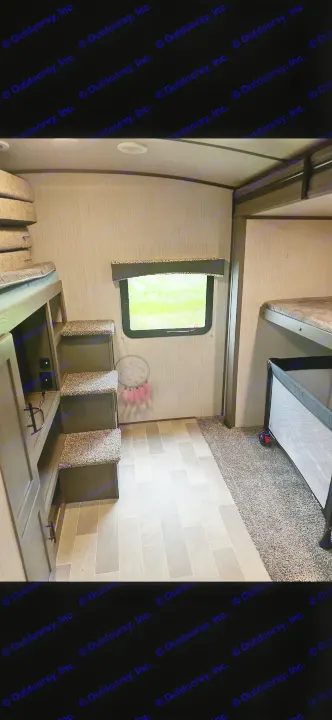Interior of an RV rental bunk room: multiple beds with steps, a window showing greenery, and a portable baby crib on carpet.. Cruiser RV MPG Ultra Lite 2021