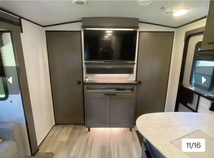 Spacious RV rental living area with a central entertainment unit, TV, soundbar, flanking storage doors, and modern kitchen access.. Cruiser RV MPG Ultra Lite 2021