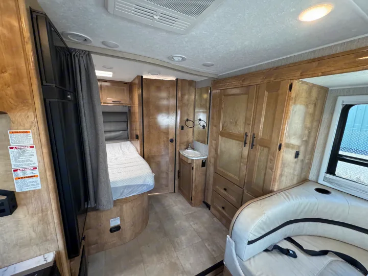 RV rental interior showing a cozy bed, compact bath area, seating, and ample storage cabinets.. Coachman Prism Select 24 CB 2021