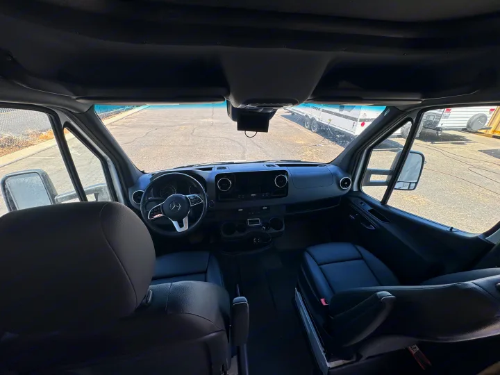 RV rental interior showing the driver's cockpit, steering wheel, dashboard, and view of parked RVs.. Coachman Prism Select 24 CB 2021