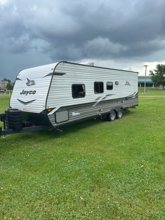 A Jayco travel trailer, an excellent RV rental option, parked on a grassy field under dark, stormy clouds.. Jayco Jay Flight SLX 2022
