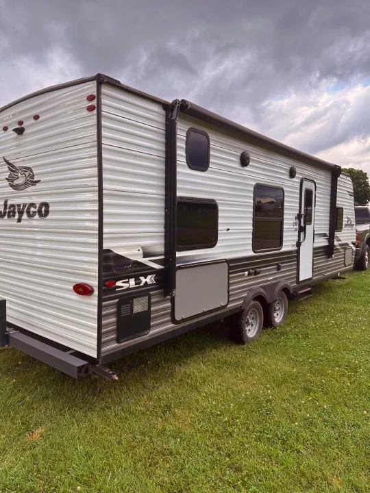 Jayco travel trailer RV rental parked on green grass under cloudy skies, ready for your next adventure.. Jayco Jay Flight SLX 2022