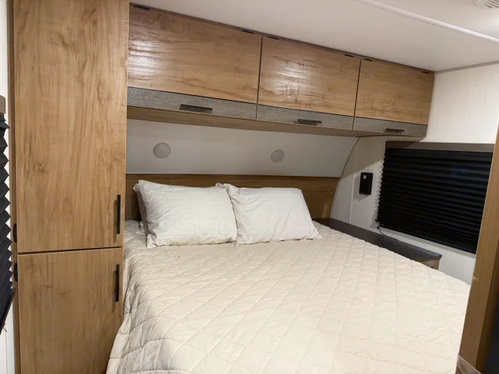 Inviting RV rental bedroom: light wood cabinets, comfortable bed with quilted bedding, and window.. Forest River Campsite reserve 26CJ 2025