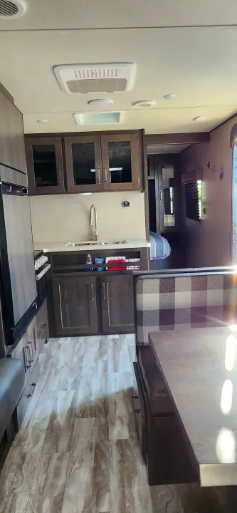 Clean RV rental interior featuring a compact kitchen with sink, dinette seating, and hallway leading to a bedroom. Light wood flooring.. Grand Design Transcend Xplor 2022