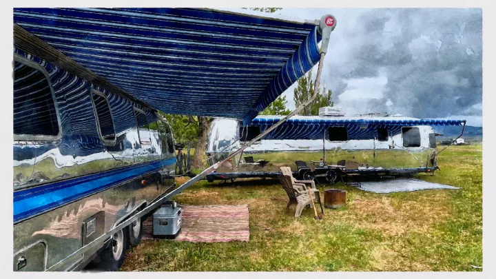 Two shiny Airstream RVs with blue awnings extended, set up for camping. Consider an RV rental!. Airstream Excella 1990