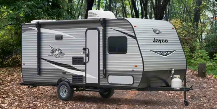 Explore nature with this gray Jayco Jay Flight SLX travel trailer, perfect for an RV rental parked in a lush forest campsite.. Jayco Jay Flight SLX 2021